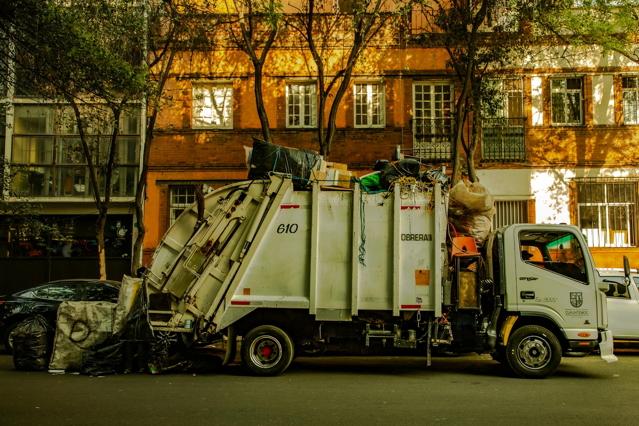Garbage truck parked on an urban street in daylight, with residential buildings in the background.